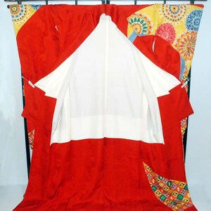 May include: A red and white kimono with a colourful floral pattern. The kimono is open to reveal the white lining. The kimono is hanging on a black stand.