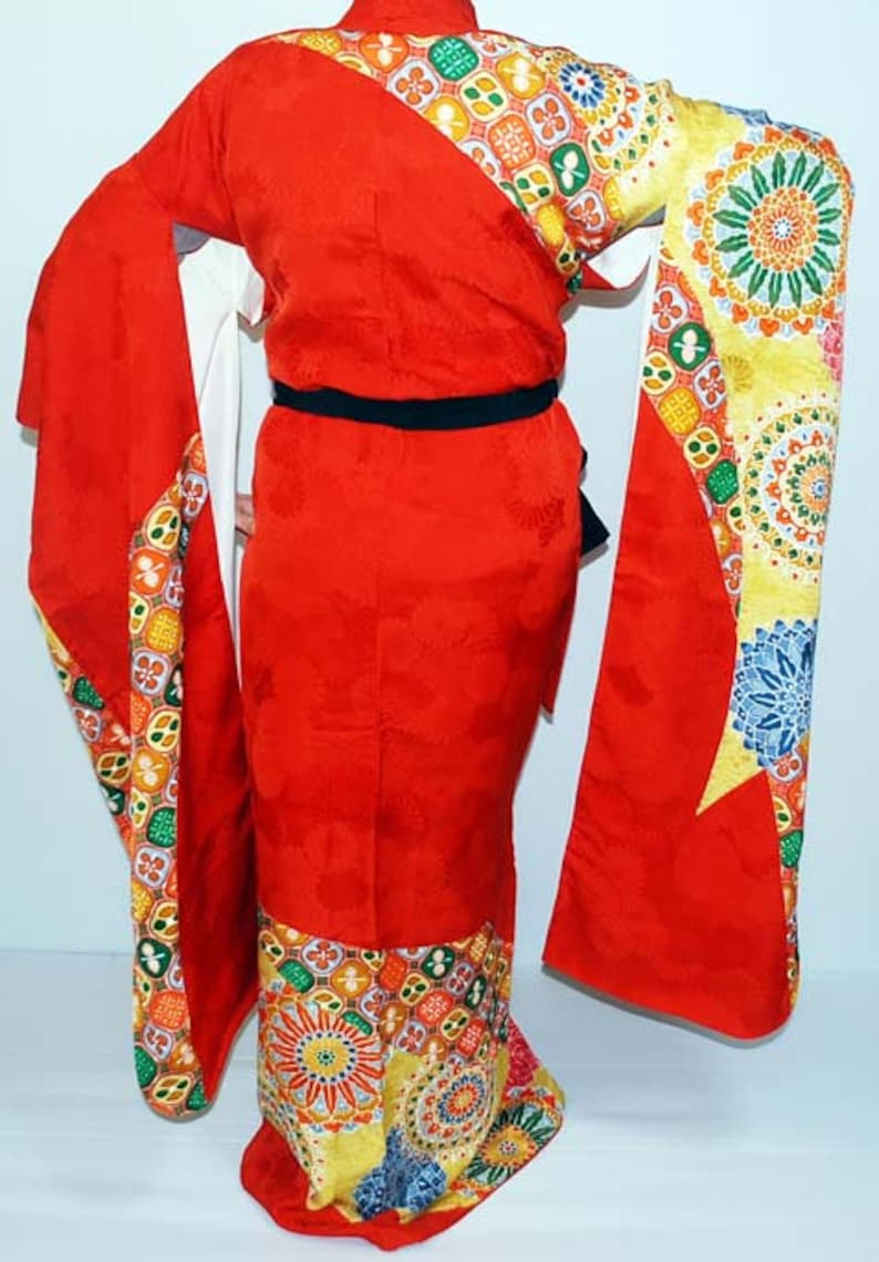 May include: A red kimono with a colourful geometric pattern. The kimono has long sleeves and a sash.