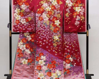 May include: A deep red kimono featuring an intricate floral pattern with white, orange, and yellow blossoms. The garment displays a gradient effect toward the bottom, transitioning into a lighter pink hue with purple accents and detailed embroidery.