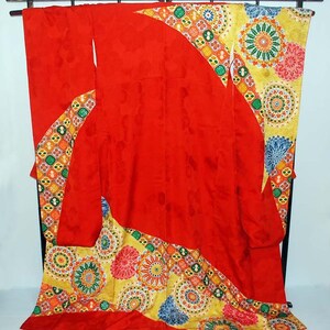 May include: A red kimono with a colourful geometric pattern. The kimono is displayed on a wooden stand.