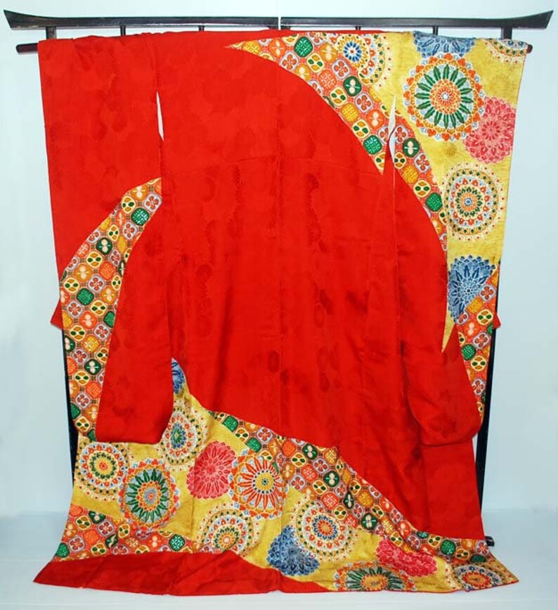 May include: A red kimono with a colourful geometric pattern. The kimono is displayed on a wooden stand.