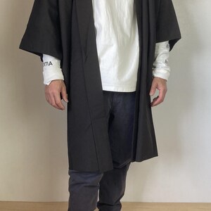 May include: A black kimono-style robe with long sleeves and a white t-shirt underneath. The person is wearing black pants and is barefoot.