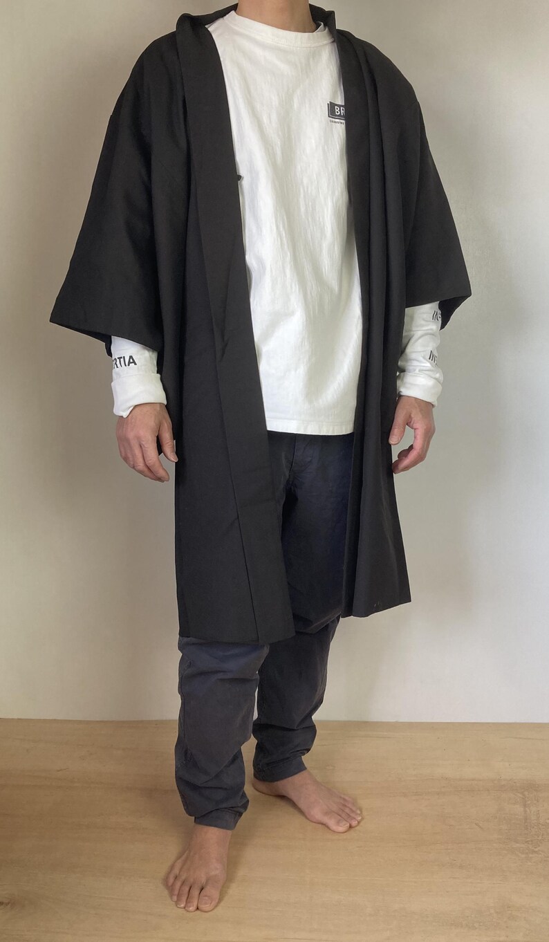 May include: A black kimono-style robe with long sleeves and a white t-shirt underneath. The person is wearing black pants and is barefoot.
