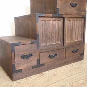 May include: A dark brown wooden cabinet with multiple drawers and doors. The cabinet has a stepped design and features black metal accents.