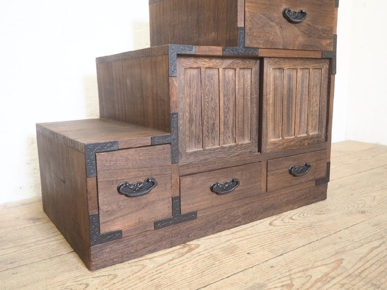 May include: A dark brown wooden cabinet with multiple drawers and doors. The cabinet has a stepped design and features black metal accents.