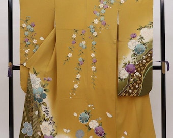 May include: A yellow kimono with a floral pattern. The kimono has a long, flowing design with a variety of flowers in shades of purple, blue, and white. The kimono is displayed on a black stand.