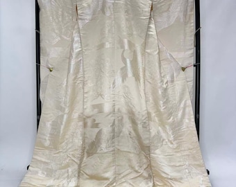 May include: Ivory-colored kimono with a crane pattern. The traditional Japanese garment is displayed on a black stand. The fabric has a subtle sheen, and the crane design is visible throughout the garment.