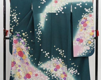 May include: A dark teal kimono with a floral design. The kimono features a gradient of colors, with white, pink, yellow, and purple flowers. The garment is displayed on a black metal rack.