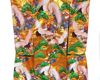 May include: A gold-colored kimono with a vibrant design featuring white cranes with outstretched wings, green foliage, and colorful floral accents. The kimono has a red border at the bottom and is likely made of silk or a similar luxurious fabric.
