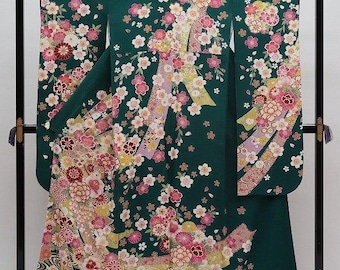 May include: A dark green kimono with a floral pattern of pink, white, and yellow blossoms. The kimono is displayed on a black stand, showcasing its intricate design and traditional style. The floral pattern is spread across the entire garment.