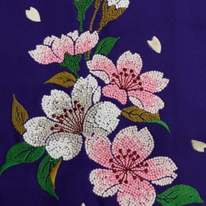 May include: Embroidered cherry blossoms in shades of pink, white, and green on a deep purple fabric background. The flowers are detailed with small beads and the leaves are a vibrant green.