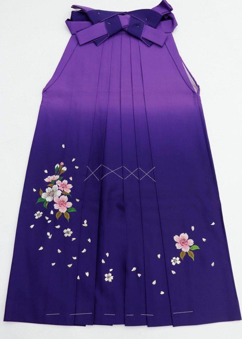 May include: A purple and white hakama with a gradient design and embroidered cherry blossoms. The hakama is a traditional Japanese garment worn by both men and women.
