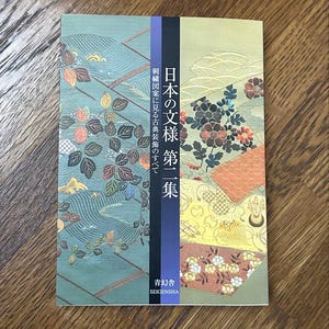Pode incluir: Um livro intitulado "Padrões japoneses, Volume 1" com texto japonês e desenhos florais. A capa apresenta um esquema de cores verde-azulado, dourado e laranja com padrões intrincados. Publicado por Seigensha.