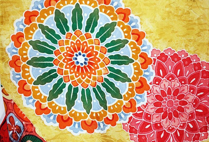 May include: A yellow fabric with a large orange, red and blue floral design. The design is surrounded by green leaves. A smaller pink floral design is in the bottom right corner.