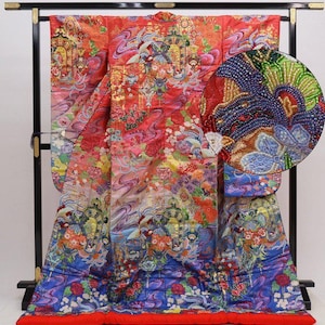 May include: A vibrant, ornate Japanese kimono, predominantly red with intricate floral and wave patterns. The design incorporates shades of pink, blue, and gold, with a detailed close-up showcasing embroidered elements. The kimono is displayed on a black stand.