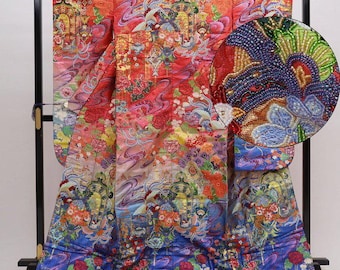 Könnte beinhalten: Ein reich verziertes japanisches Kimono, hauptsächlich rot, mit komplizierten Blumen- und Wellenmustern. Das Design enthält Schattierungen von Rosa, Blau und Gold, mit einer detaillierten Nahaufnahme, die gestickte Elemente zeigt. Das Kimono wird auf einem schwarzen Ständer präsentiert.