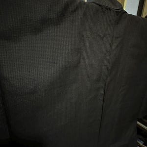 May include: A dark brown kimono with a textured weave. The kimono is hanging on a hanger and is folded in half.