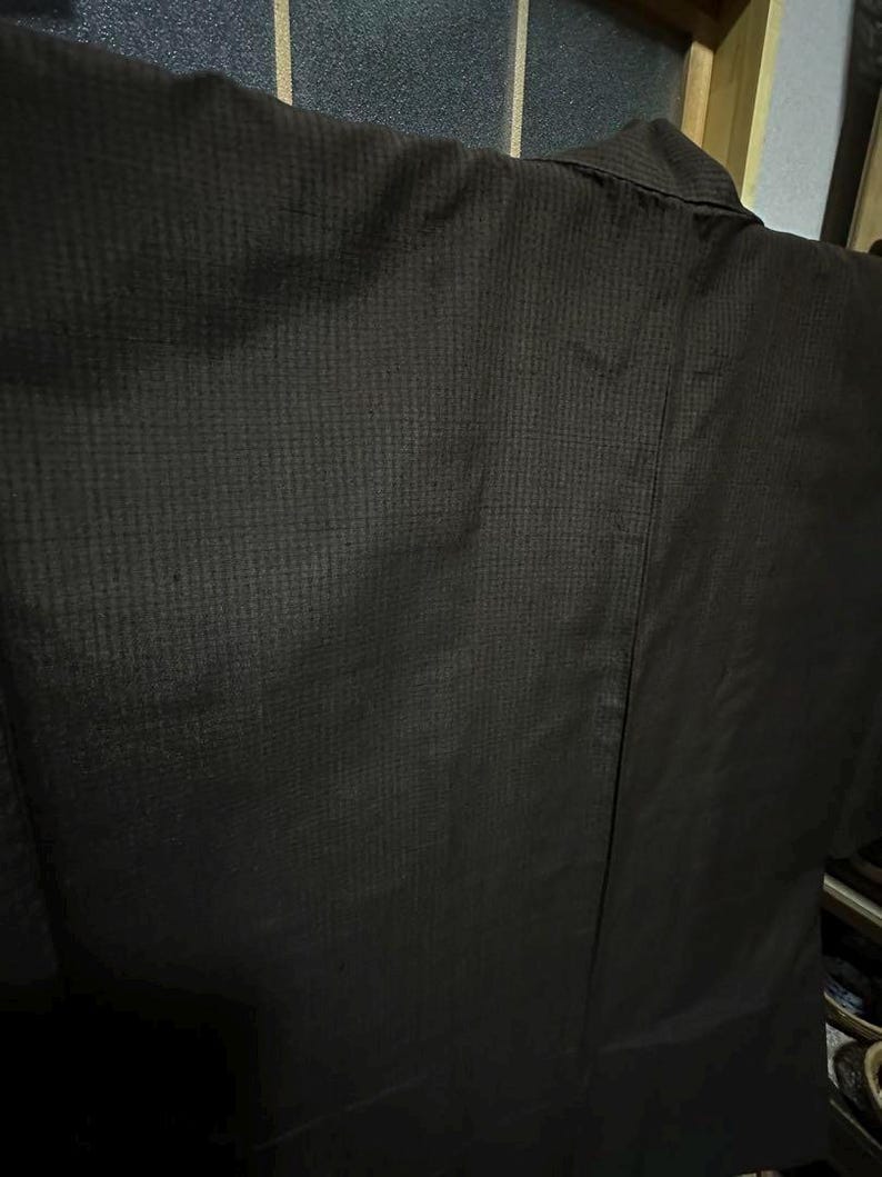 May include: A dark brown kimono with a textured weave. The kimono is hanging on a hanger and is folded in half.