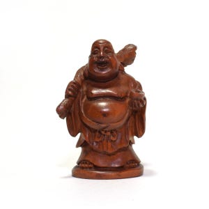 May include: A carved wooden figurine of a smiling, rotund figure with a large belly, wearing loose robes. The figure holds a sack over one shoulder and a small bowl in the other hand, featuring a polished, medium-brown wood grain finish throughout.