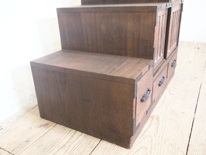 May include: A dark brown wooden step stool with three tiers and two drawers. The drawers have black metal handles.