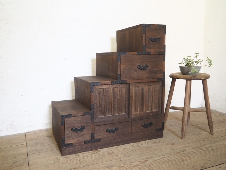 May include: A dark brown wooden cabinet with multiple drawers and doors. The cabinet is stacked in a stepped design, creating a unique and decorative piece of furniture.