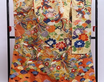 May include: A traditional Japanese kimono with a gold background and intricate embroidery of colorful birds and flowers. The kimono is displayed on a black stand.