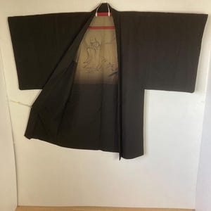 May include: A black Japanese kimono with a light brown lining featuring a printed design of a person in a robe.