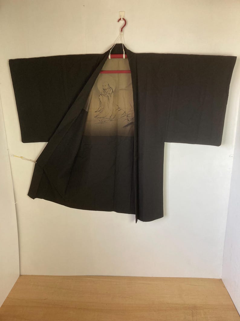May include: A black Japanese kimono with a light brown lining featuring a printed design of a person in a robe.