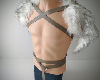 May include: A chest harness featuring taupe-colored faux leather straps that cross over the torso, accented with white and grey faux fur shoulder pieces. The harness includes a waist strap secured with a silver-toned metal ring buckle.