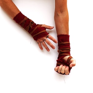 Puede incluir: Un par de mu&ntilde;equeras de tela roja con correas de cuero marr&oacute;n. Las mu&ntilde;equeras est&aacute;n atadas alrededor de las mu&ntilde;ecas y aseguradas con nudos.