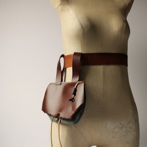 May include: A brown leather bag with a flap and a drawstring closure. The bag is attached to a brown leather belt.