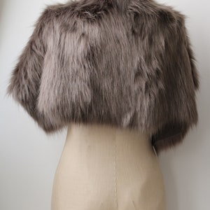 May include: A gray faux fur shrug with a short, cropped length. The shrug is displayed on a mannequin against a white background.