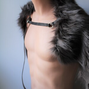 May include: A gray faux fur shoulder wrap with a gray leather strap and silver hardware. The wrap is displayed on a mannequin.