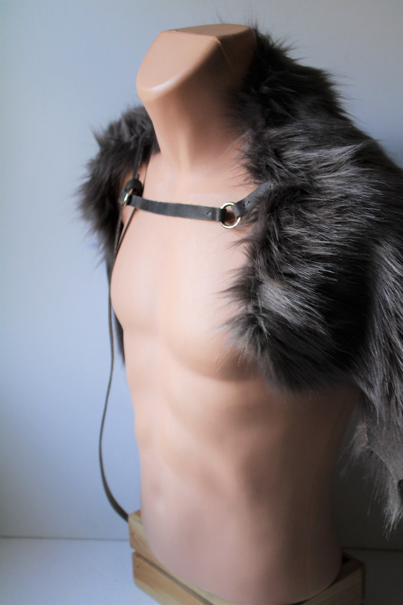 May include: A gray faux fur shoulder wrap with a gray leather strap and silver hardware. The wrap is displayed on a mannequin.
