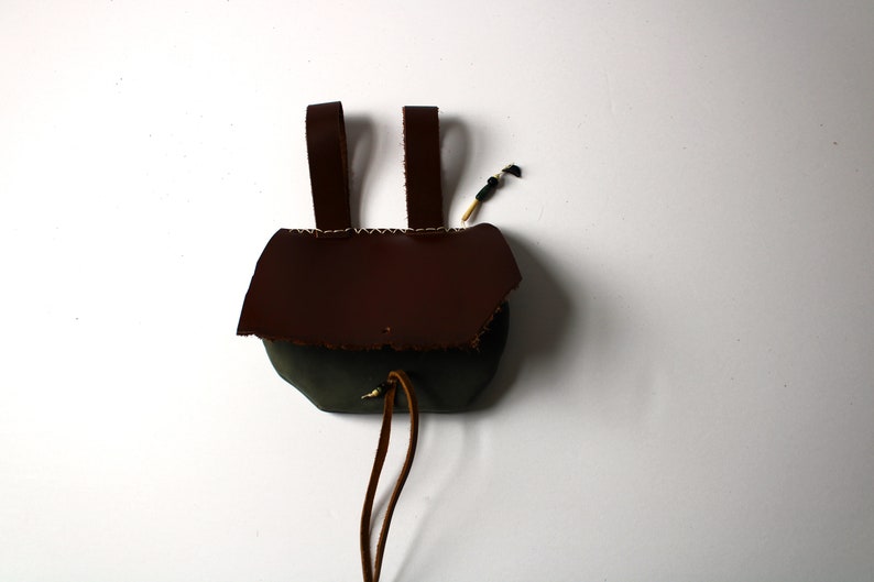 May include: A small brown leather pouch and a drawstring closure. The pouch has two leather straps for carrying.