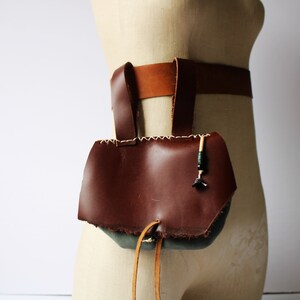May include: A brown leather pouch with a drawstring closure and a decorative beaded strap. The pouch is attached to a brown leather belt.