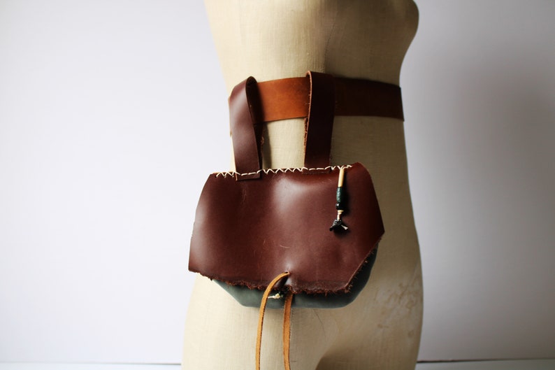 May include: A brown leather pouch with a drawstring closure and a decorative beaded strap. The pouch is attached to a brown leather belt.