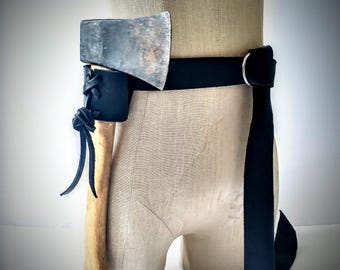 May include: A black leather belt with a silver buckle holds a small axe in a black leather sheath. The axe has a wooden handle and a silver head. The belt is displayed on a mannequin.