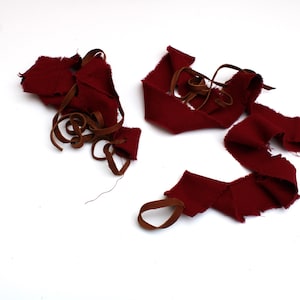 Puede incluir: Un mont&oacute;n de retazos de tela roja con correas de cuero marr&oacute;n. La tela est&aacute; deshilachada y rasgada, lo que sugiere que se cort&oacute; de una pieza m&aacute;s grande.