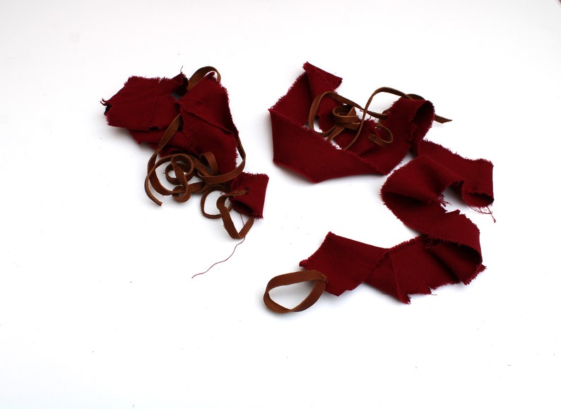 Puede incluir: Un mont&oacute;n de retazos de tela roja con correas de cuero marr&oacute;n. La tela est&aacute; deshilachada y rasgada, lo que sugiere que se cort&oacute; de una pieza m&aacute;s grande.