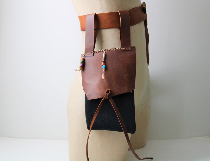 May include: A brown leather belt with a brown leather pouch attached. The pouch has a drawstring closure. The belt has a decorative beaded strap with colorful beads.
