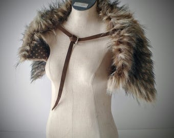 May include: A faux fur shoulder wrap featuring long, multi-tonal brown and black fibers. The garment is secured with a thin brown leather strap and a silver-toned metal buckle. The interior lining is brown fabric with a white polka dot pattern.