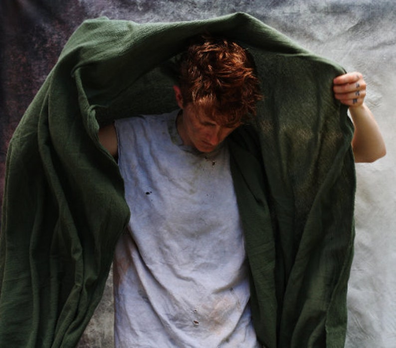 the drab green shawl is aloft, being pulled up over the wearers head and shoulders. the cotton is lightweight and airy