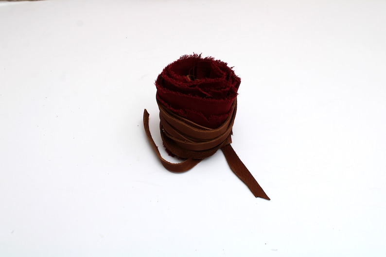 Puede incluir: Un rollo de cinta de tela color burdeos atado con una cinta de cuero marr&oacute;n.
