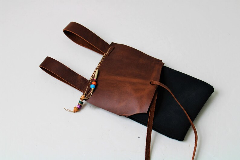bag has two loops to hang from your belt and a brown flap. the stitch trim and ornamental beads are visible