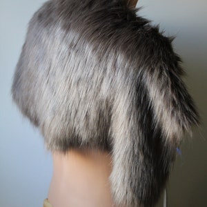May include: A gray faux fur stole with a long, flowing design. The stole is displayed on a mannequin against a white background.
