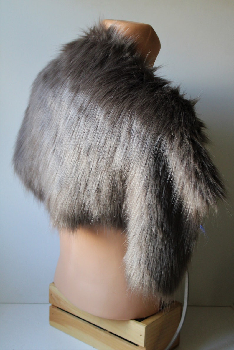 May include: A gray faux fur stole with a long, flowing design. The stole is displayed on a mannequin against a white background.