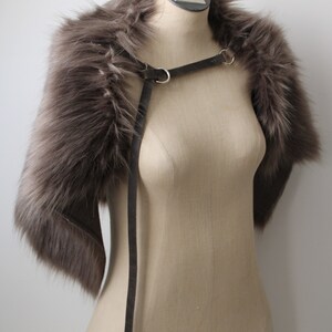 May include: A gray faux fur stole with a black leather strap and silver buckles. The stole is displayed on a mannequin.