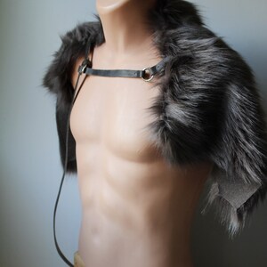 May include: A gray faux fur shoulder wrap with a black leather strap and a gold metal ring. The wrap is displayed on a mannequin against a white background.