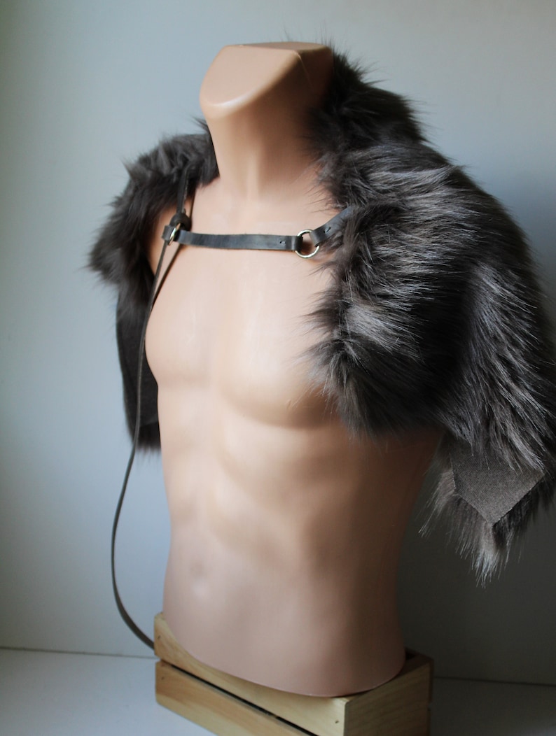 May include: A gray faux fur shoulder wrap with a black leather strap and a gold metal ring. The wrap is displayed on a mannequin against a white background.